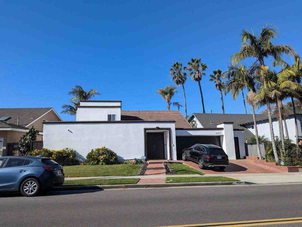 The funded Huntington Beach residence: a white two-story home with palms and a brick drive.
